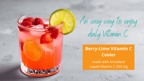Glass of berry lime cooler with raspberries, a sliced strawberry, lime slices, and AnnaKare Liquid Vitamin C on a concrete counter