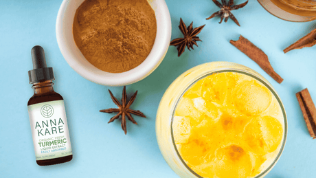 Iced golden milk latte in a glass with ice, served with a small bowl of cinnamon, a honey jar, and AnnaKare Organic Fresh Turmeric Liquid Extract
