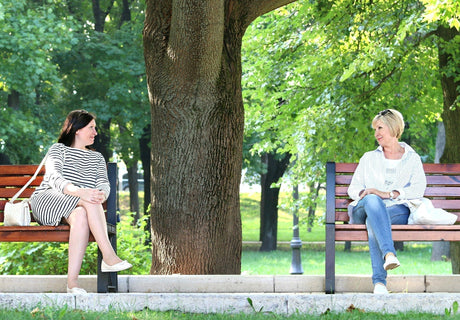 Two healthy women over 50 sitting on a park bench and talking outdoors, reflecting a natural wellness approach to bone health.